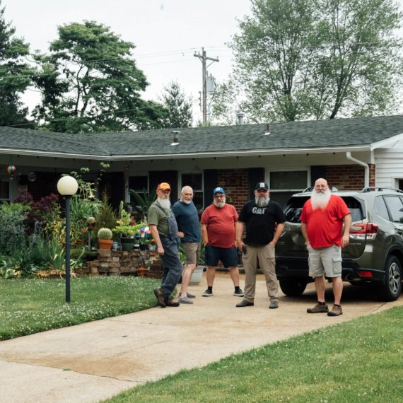 Bearded men stand in front of a ranch style house