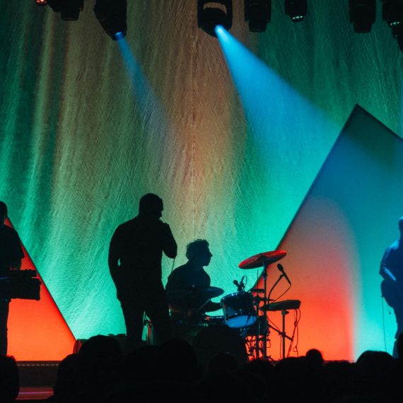 Future Islands performs silhouetted agains a colorful geometric backdrop of shapes on a stage