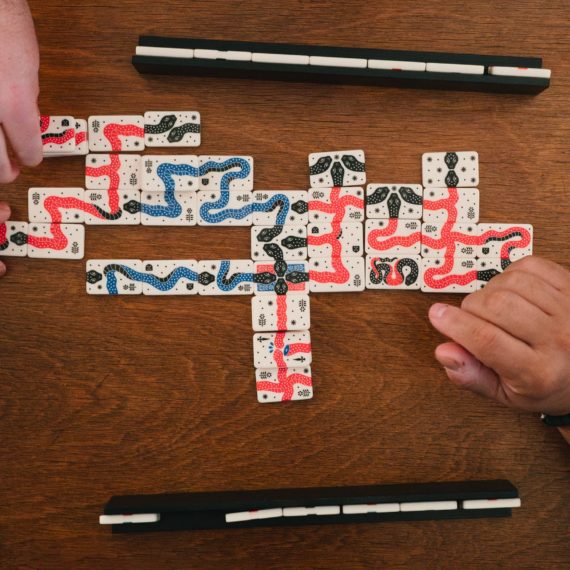 Two folks arrange red and blue snake tiles on a table top