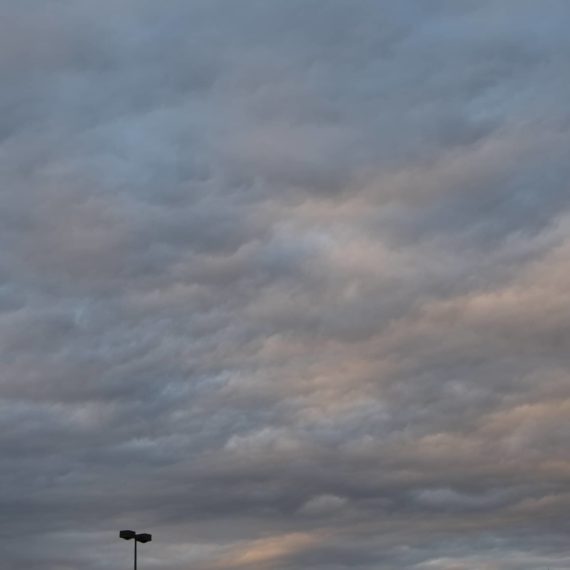 Painterly clouds in the sky with a tiny sliver of parking lot lights on the bottom edge