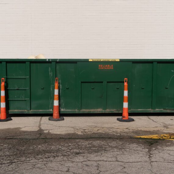 A green dumpster with orange cones